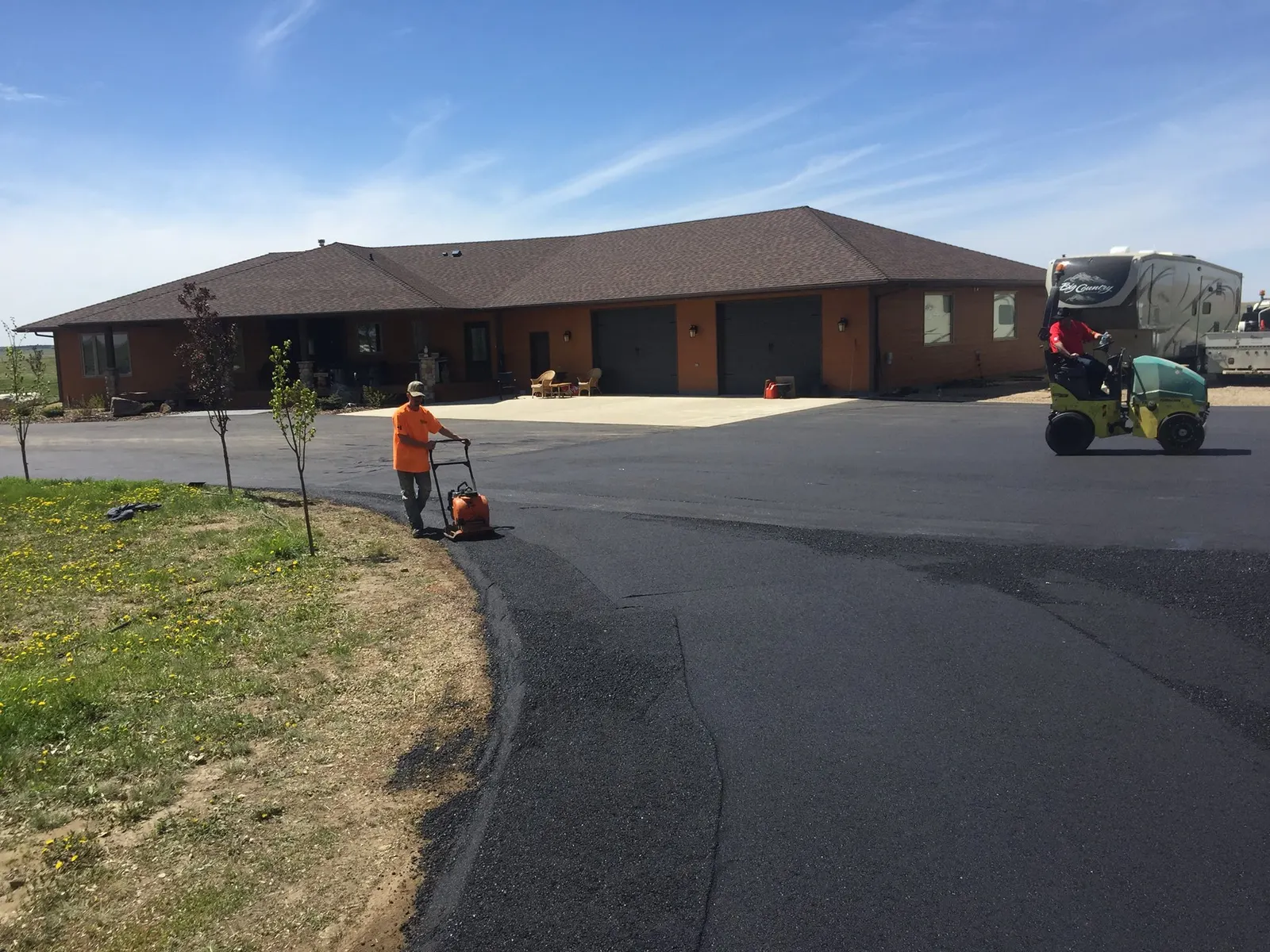 Workers compacting and rolling a freshly paved asphalt driveway on a sunny day